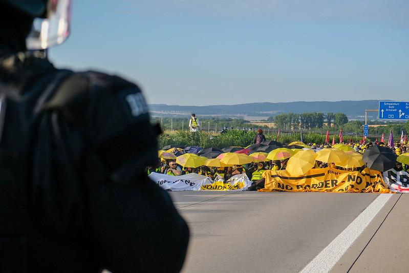 Eine Sitzblockade auf der Straße. Davor die Polizei, dahinter Hunderte Menschen mit gelben und schwarzen Schirmen. Ein Bild dafür, wie entschlossener Protest aussieht.

CC BY-NC 4.0 @jonasertle
